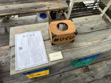 たまれ万博入口手前に置かれていたおじくじ説明文と質問が書かれていた用紙が入っている木箱。